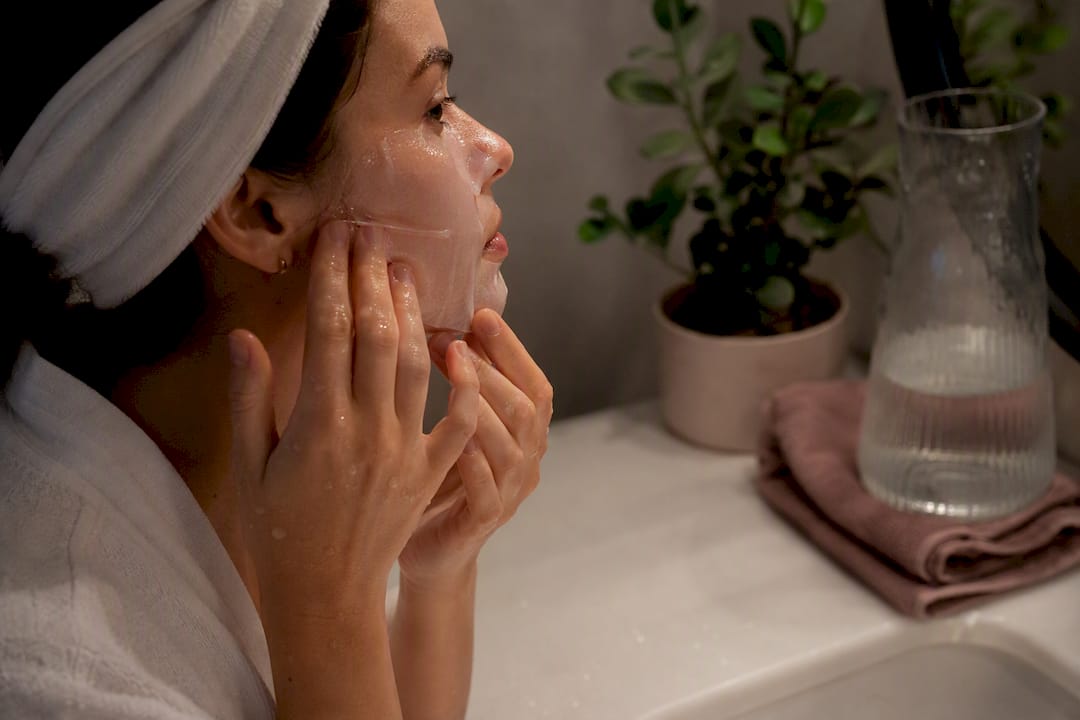 Hands applying translucent hydrogel facial mask at night