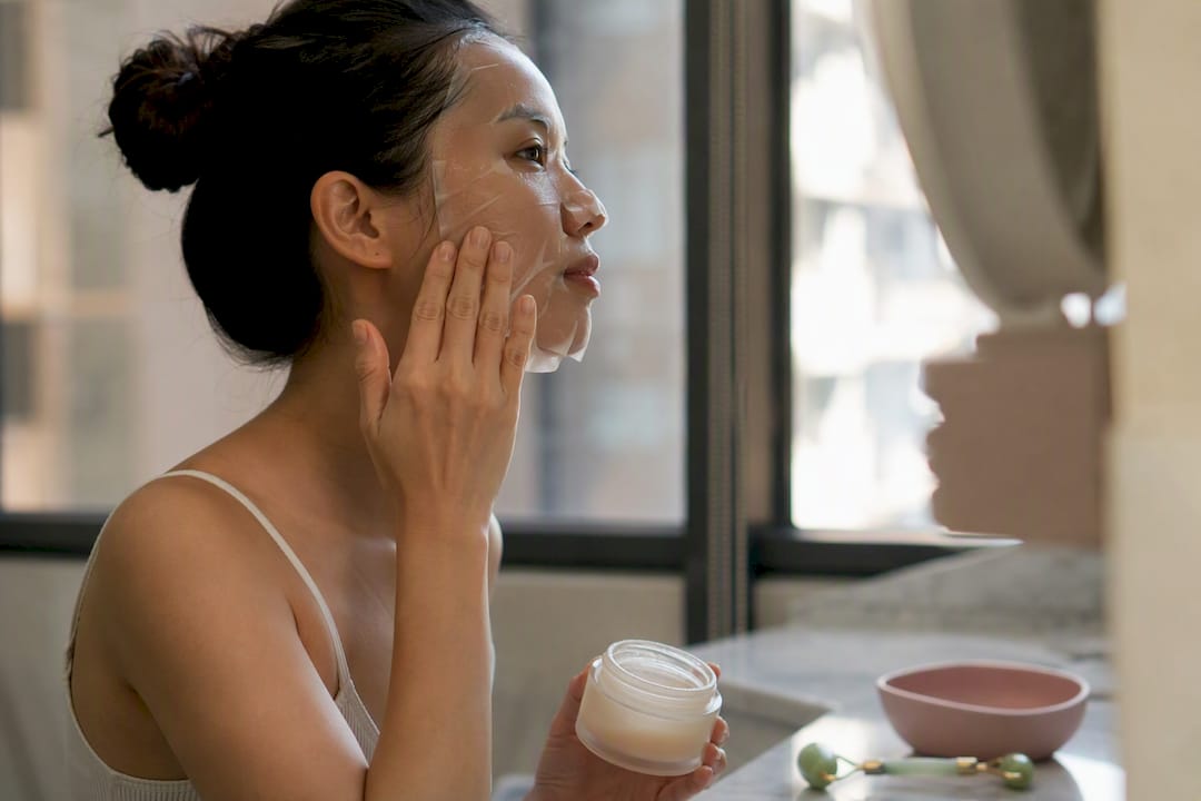 Hands applying sheet mask and holding jar mask